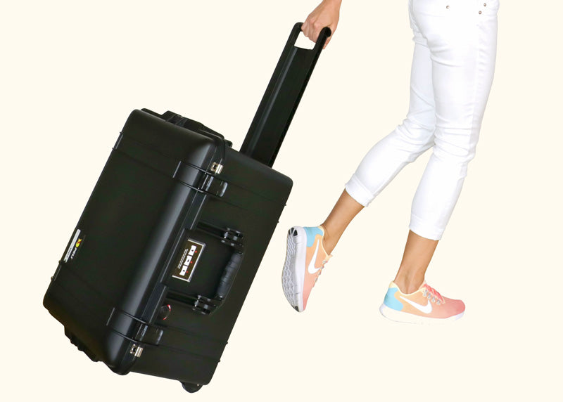 Smidig svart transportväska i hårdplast rullas av tjej i vita byxor och sneakers.
