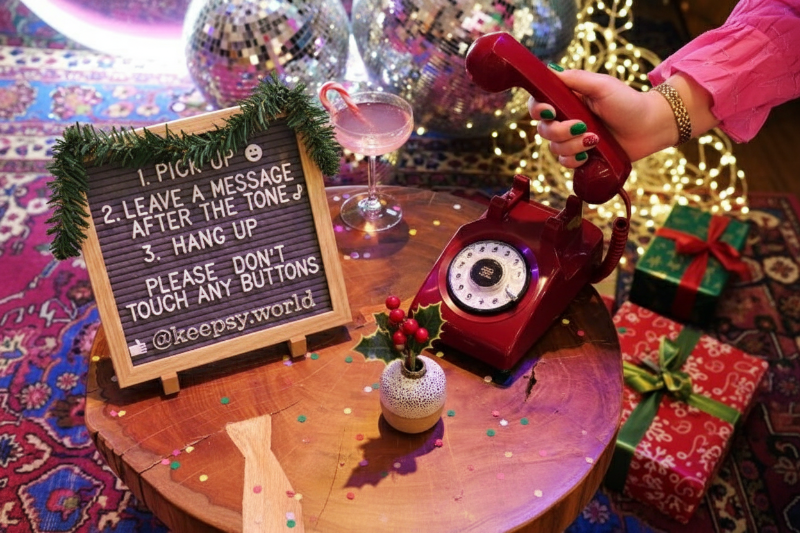 Finklädd hand lyfter luren på retro telefon i julig festmiljö.